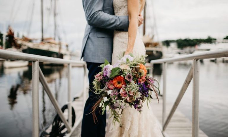 A bride and groom standing on a dock at the Camden Harbor. Photo Credit: Lindsay Vann Photography